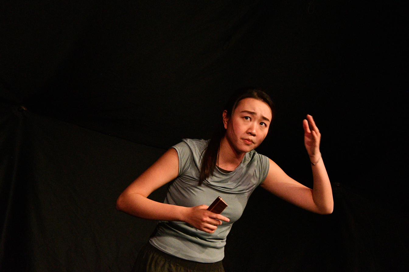A performer gestures, caught in a moment of memory, against black.