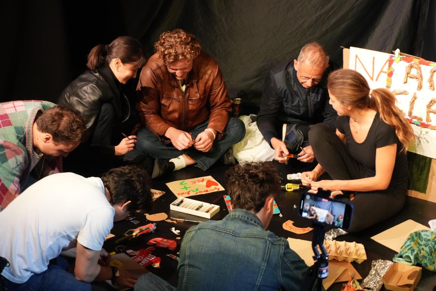 Audience members sit in a circle after the show, making art from discarded materials.