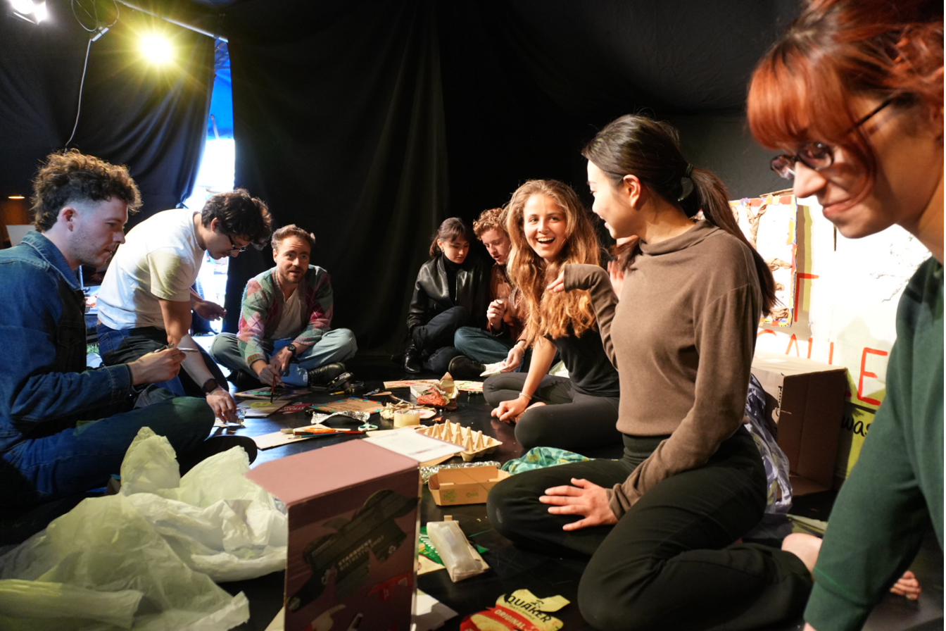 The company and workshop participants laugh together while making art from waste materials.