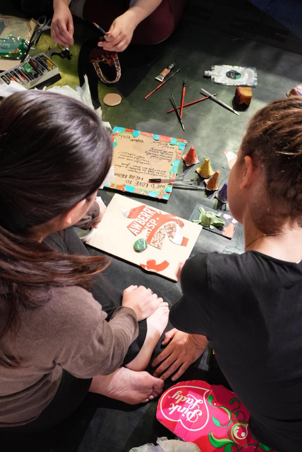 Seen from above, two participants assemble a collage from packaging.