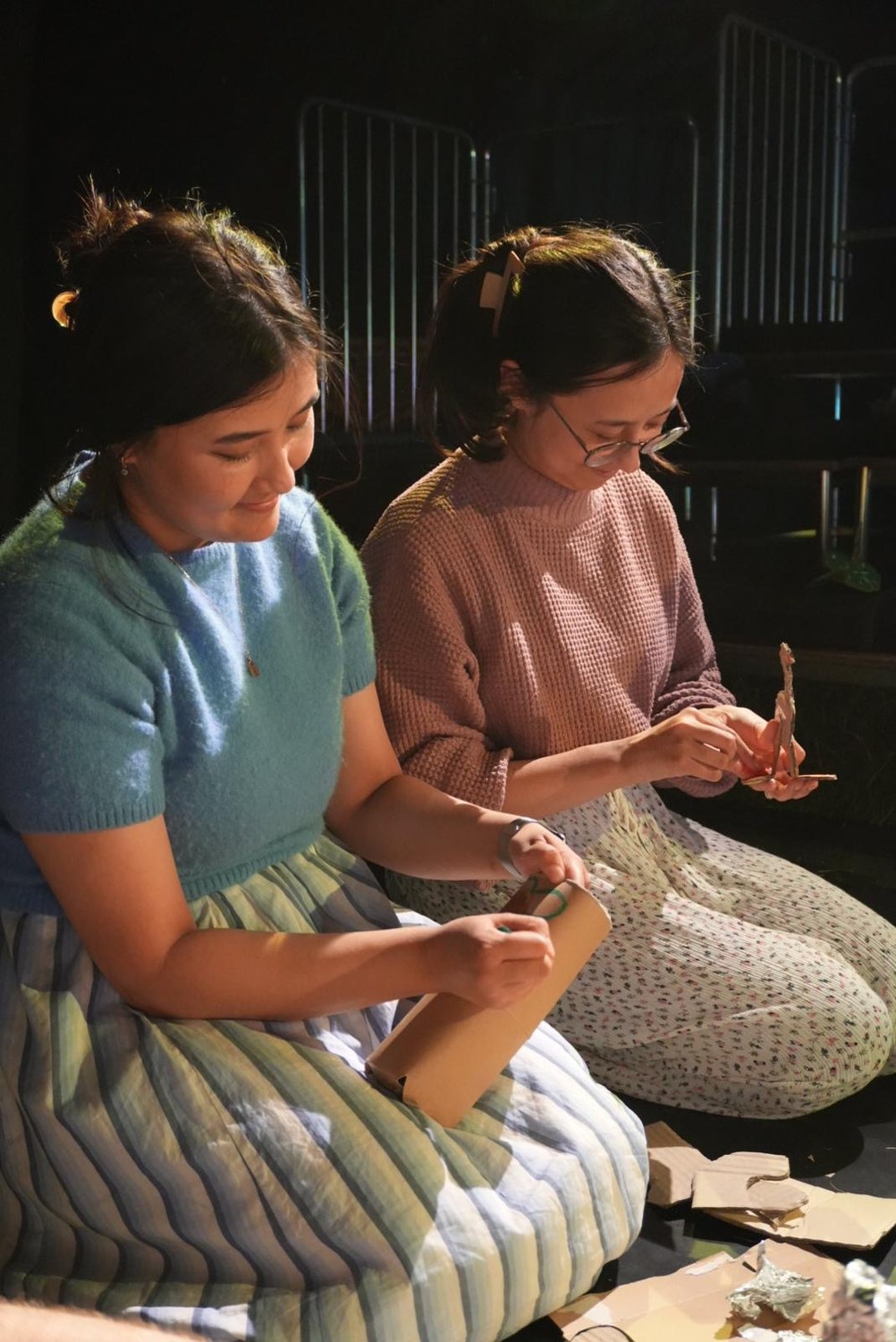 Two participants sit side by side, shaping cardboard into small sculptures.